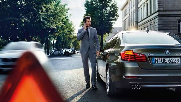 BMW Roadside Assistance BMW Roadside Assistance man on the phone in front of a BMW