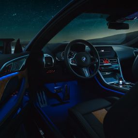Interior BMW M8 Competition Coupé F92. BMW M8 Competition Coupé, interior at night with M leather steering wheel and blue ambient light with open driver door F92.