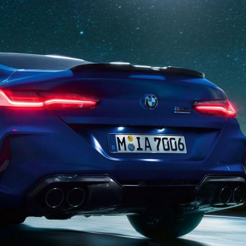 M diffuser in Carbon Black F92. BMW M8 Competition Coupé in Marina Bay Blue metallic, close-up rear at night with M diffuser in Carbon Black F92.