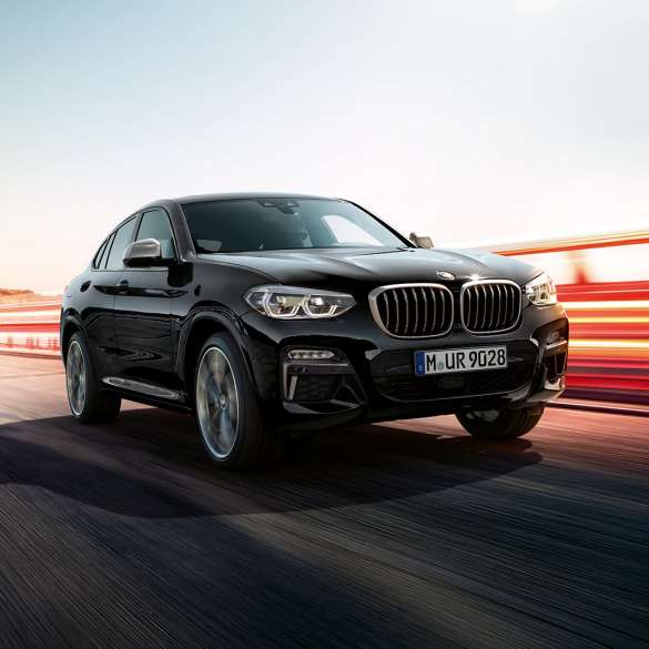 BMW X4 M40i SUV, three-quarter rear view G02. BMW X4 M40i SUV in Black Sapphire metallic, driving, exterior, three-quarter rear view with light strips G02.