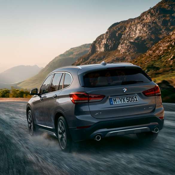 BMW X1 SUV F48, three-quarter rear view. BMW X1 SUV F48, three-quarter rear view driving in front of mountain scenery.