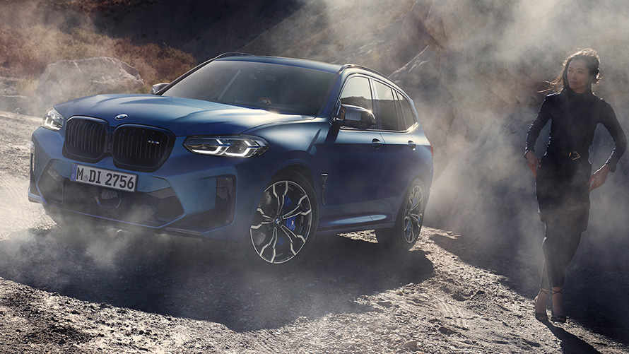 BMW X3 M 컴피티션 F97 LCI 페이스리프트 2021 프로즌 마리나 베이 블루 메탈릭 3/4 정면도, 돌이 많은 지형에 서 있는 여성 모델