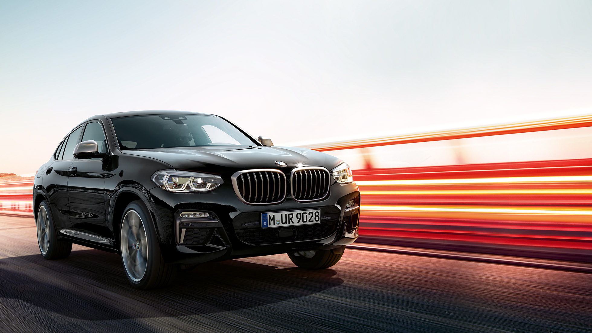 BMW X4 M40i SUV, three-quarter rear view G02. BMW X4 M40i SUV in Black Sapphire metallic, driving, exterior, three-quarter rear view with light strips G02.