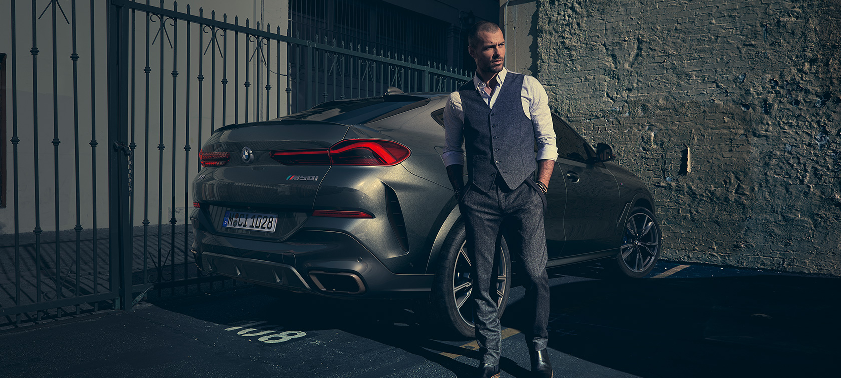 BMW X6 M50i SUV G06 in three-quarter rear view Man standing next to BMW X6 M50i SUV G06 in three-quarter rear view
