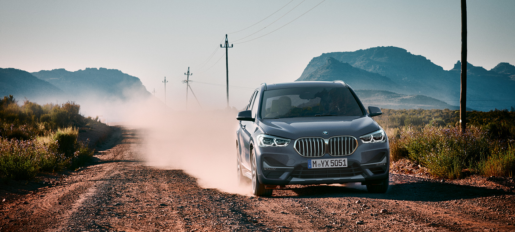 BMW X1 SUV F48, three-quarter rear view. BMW X1 SUV F48, three-quarter rear view driving in front of mountain scenery.