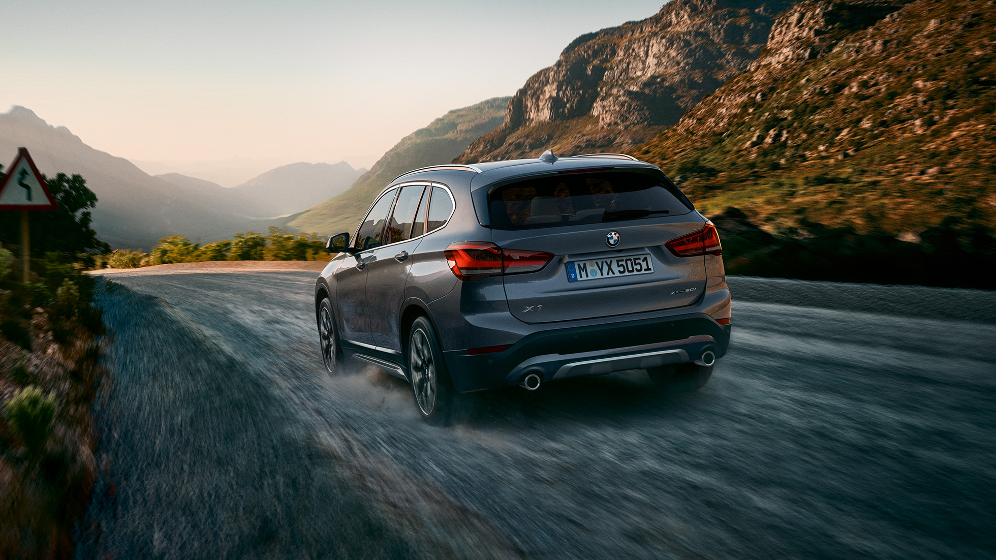 BMW X1 SUV F48, three-quarter rear view. BMW X1 SUV F48, three-quarter rear view driving in front of mountain scenery.