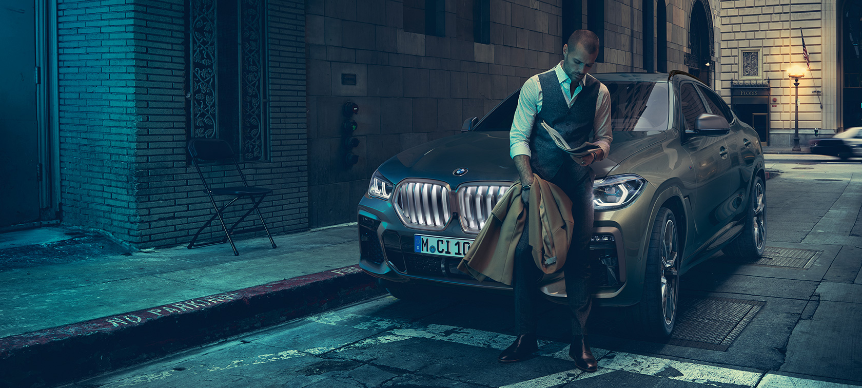 Man leaning on BMW X6 SUV G06. Man leaning on BMW X6 in lateral perspective in front of an urban setting SUV G06.